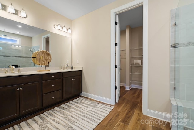 full bathroom featuring a sink, baseboards, tiled shower, and wood finished floors