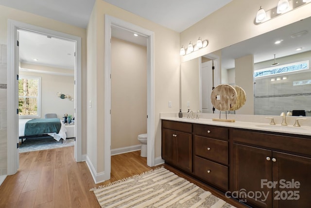 ensuite bathroom with baseboards, toilet, double vanity, wood finished floors, and a sink