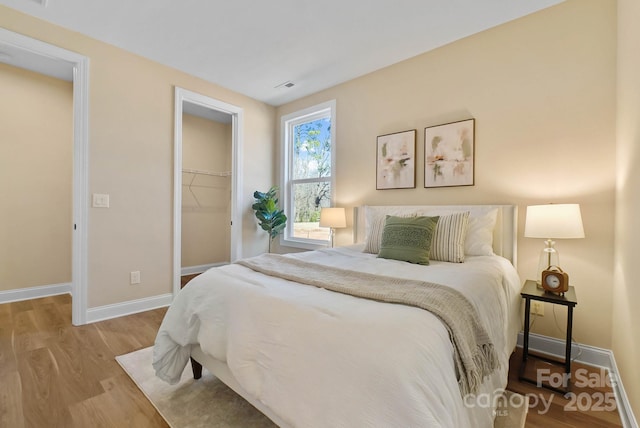 bedroom with visible vents, a walk in closet, baseboards, wood finished floors, and a closet