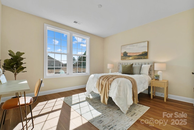 bedroom with wood finished floors, visible vents, and baseboards