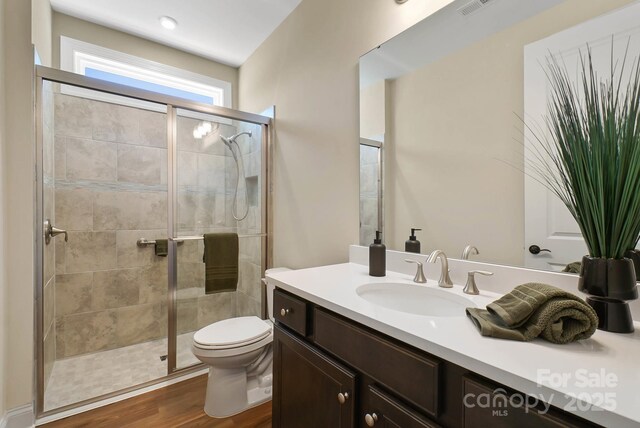 bathroom featuring a shower stall, toilet, vanity, and wood finished floors