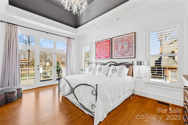 bedroom featuring access to exterior, a chandelier, a raised ceiling, and wood finished floors