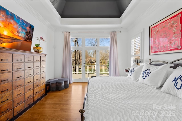 bedroom with crown molding, wood finished floors, a raised ceiling, and access to outside