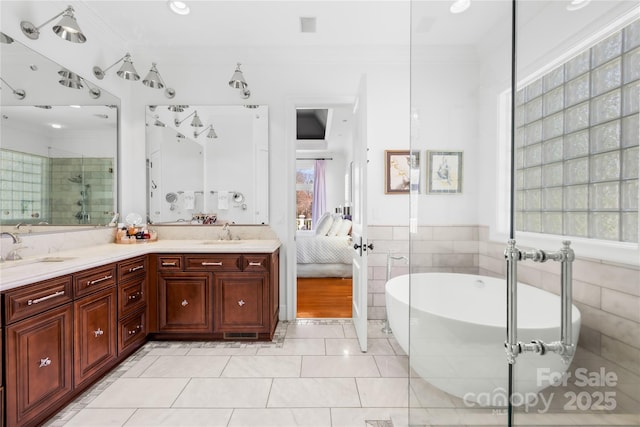 ensuite bathroom featuring connected bathroom, crown molding, double vanity, a freestanding tub, and a sink