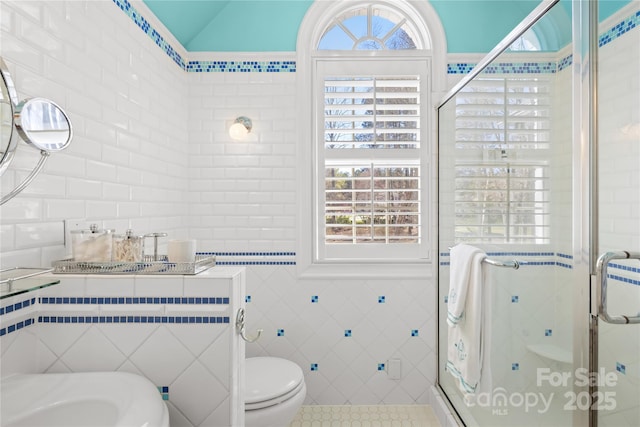 bathroom with a shower stall, toilet, lofted ceiling, tile patterned floors, and tile walls