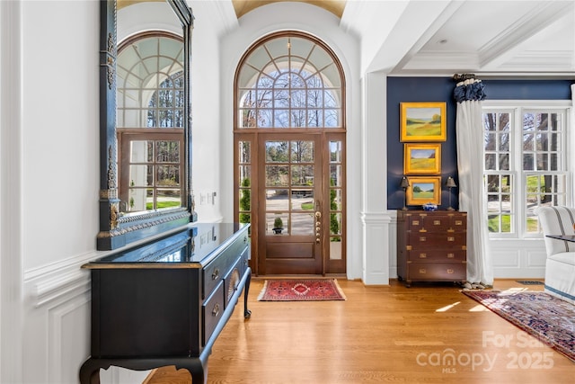 foyer entrance with a decorative wall, light wood-style flooring, crown molding, and a wainscoted wall