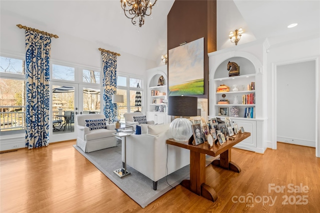 living area with built in shelves, a notable chandelier, high vaulted ceiling, wood finished floors, and french doors