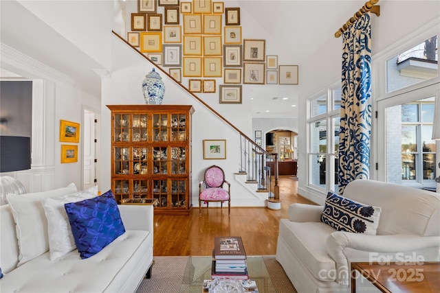 living area featuring wood finished floors, arched walkways, ornamental molding, stairs, and a towering ceiling