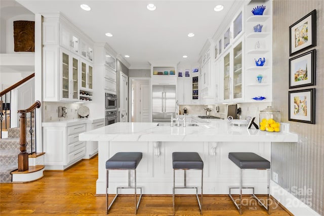 kitchen featuring stainless steel appliances, a peninsula, light wood-style flooring, and white cabinetry