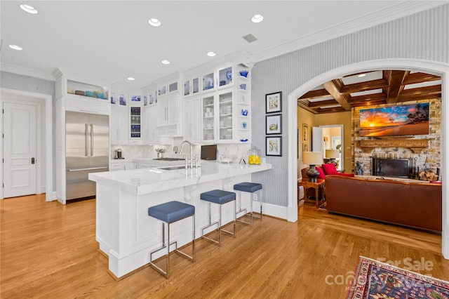 kitchen featuring built in refrigerator, a sink, arched walkways, light wood-style floors, and a peninsula