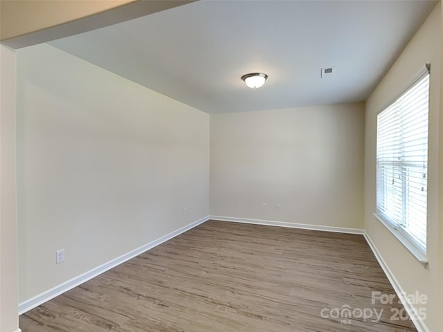 empty room featuring visible vents, wood finished floors, and baseboards