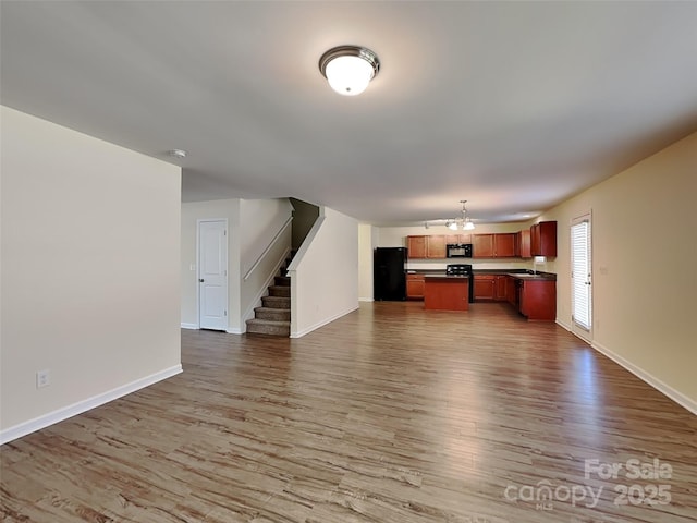 unfurnished living room with baseboards, wood finished floors, and stairs