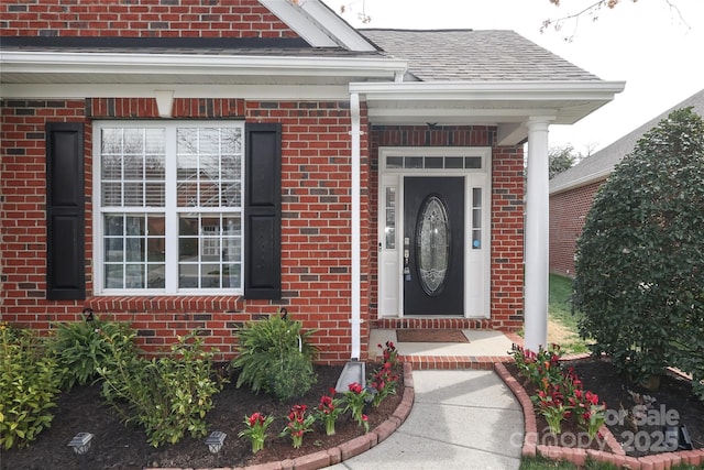 view of exterior entry featuring brick siding and a shingled roof