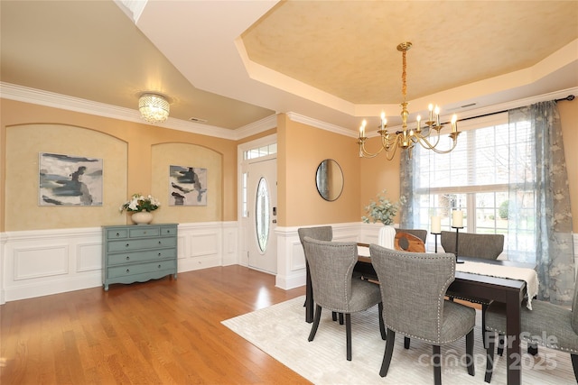 dining area featuring a wainscoted wall, a notable chandelier, wood finished floors, crown molding, and a raised ceiling