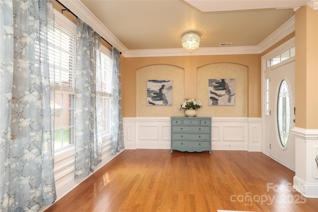 foyer entrance with plenty of natural light, wood finished floors, wainscoting, and ornamental molding