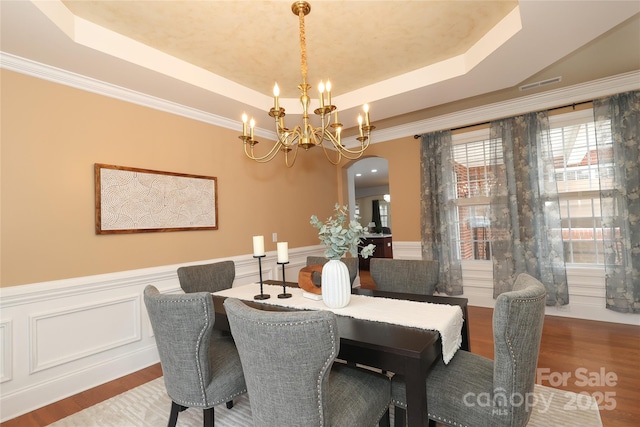 dining room with wood finished floors, a tray ceiling, arched walkways, wainscoting, and a notable chandelier