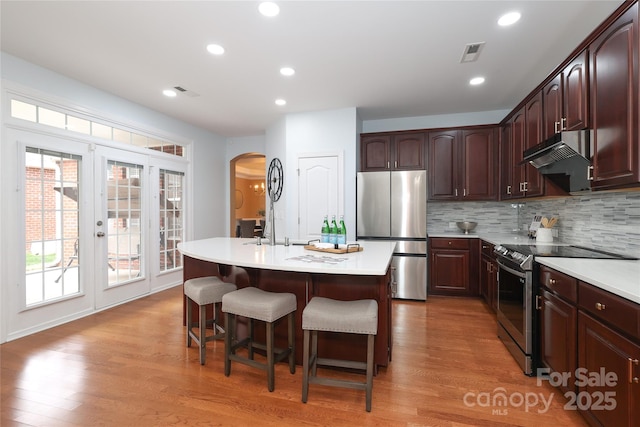 kitchen featuring under cabinet range hood, stainless steel appliances, light wood finished floors, and light countertops