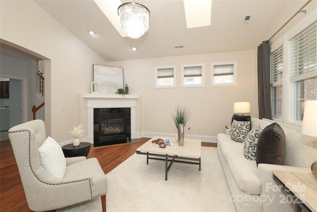 living room featuring visible vents, a fireplace with flush hearth, a notable chandelier, wood finished floors, and vaulted ceiling