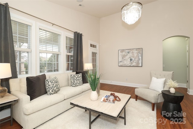 living room featuring a notable chandelier, wood finished floors, arched walkways, and baseboards