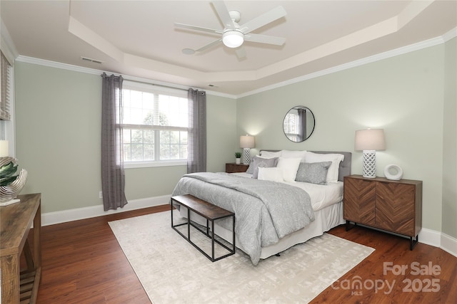 bedroom featuring visible vents, baseboards, dark wood finished floors, a tray ceiling, and ornamental molding