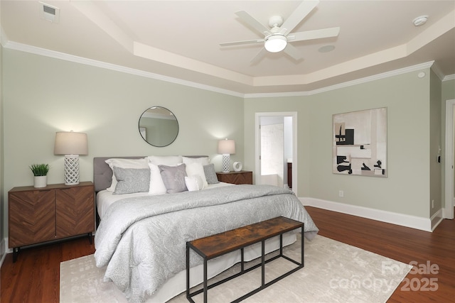 bedroom featuring wood finished floors, visible vents, baseboards, a tray ceiling, and ornamental molding