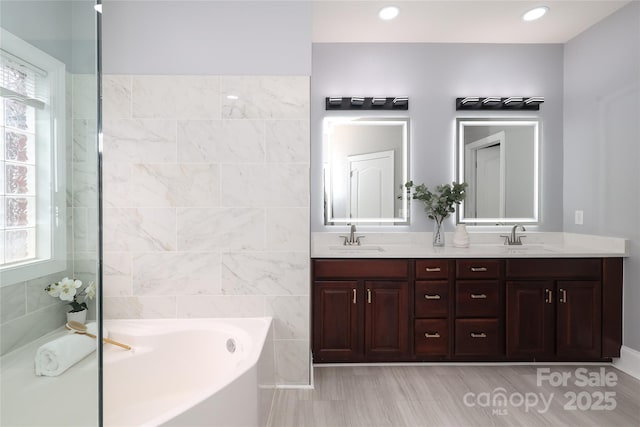 bathroom featuring a garden tub, recessed lighting, double vanity, and a sink