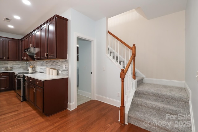 kitchen featuring electric range, visible vents, under cabinet range hood, light countertops, and decorative backsplash