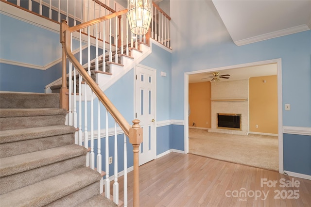 stairs featuring a brick fireplace, a ceiling fan, baseboards, and wood-type flooring