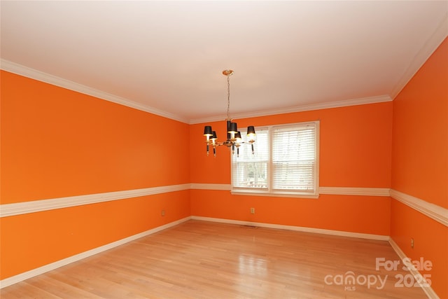 spare room featuring baseboards, an inviting chandelier, wood finished floors, and crown molding