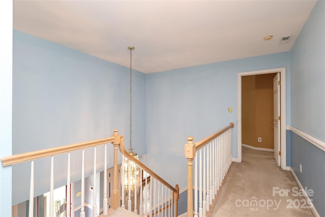 hallway featuring carpet flooring, an upstairs landing, visible vents, and baseboards