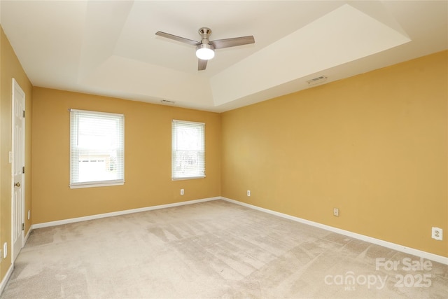 empty room featuring a tray ceiling, baseboards, light colored carpet, and visible vents