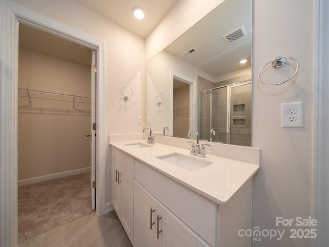 bathroom with a sink, visible vents, a spacious closet, and a shower stall