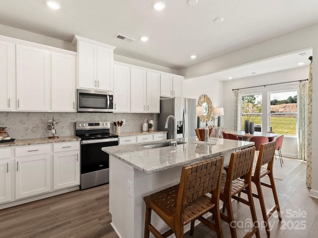 kitchen with a breakfast bar, an island with sink, a sink, backsplash, and appliances with stainless steel finishes