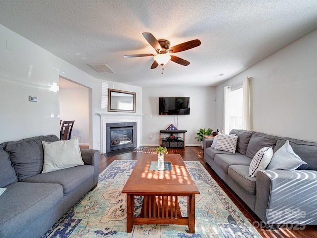 living room featuring a glass covered fireplace, a textured ceiling, wood finished floors, and a ceiling fan