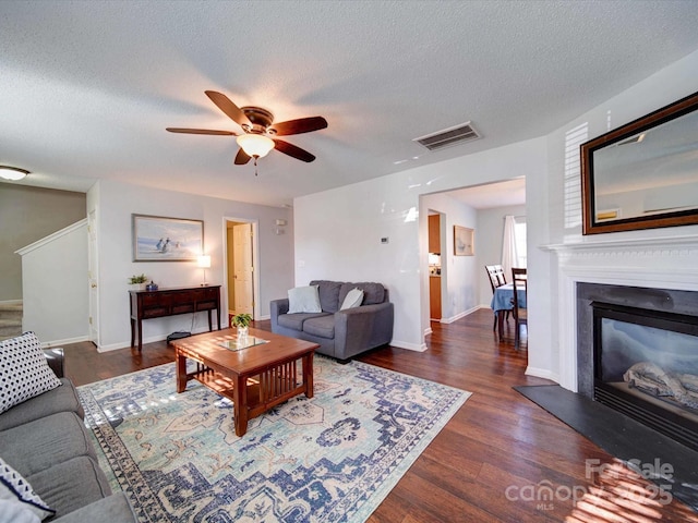 living room with a ceiling fan, wood finished floors, visible vents, a textured ceiling, and a glass covered fireplace