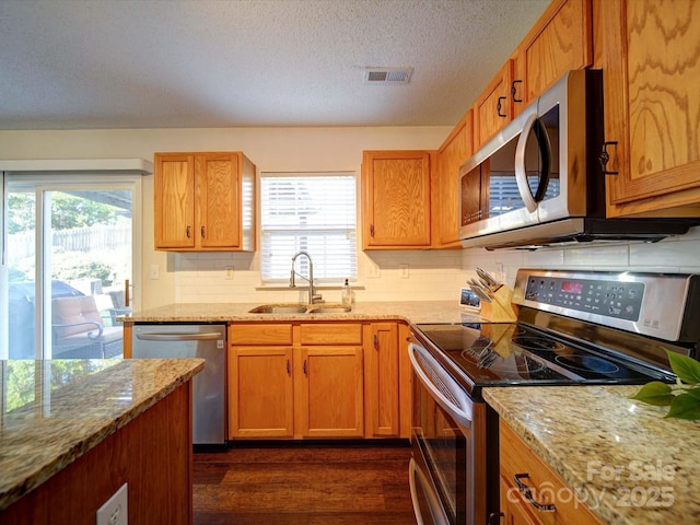 kitchen with a sink, a healthy amount of sunlight, light stone countertops, and stainless steel appliances