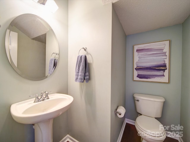 half bath with toilet, baseboards, and a textured ceiling