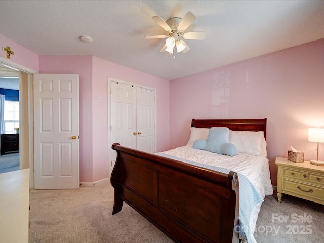 bedroom featuring a ceiling fan, a textured ceiling, a closet, baseboards, and light colored carpet