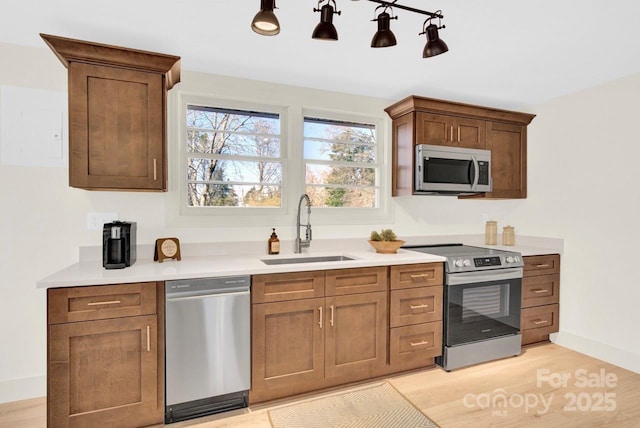 kitchen featuring a sink, stainless steel appliances, light wood-type flooring, and light countertops