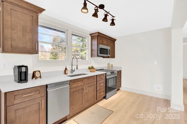 kitchen featuring baseboards, light countertops, light wood-style floors, stainless steel appliances, and a sink