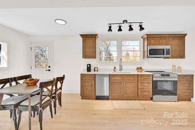 kitchen featuring light wood finished floors, brown cabinets, appliances with stainless steel finishes, and a sink