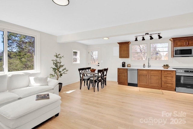 kitchen with brown cabinets, stainless steel appliances, light wood-style floors, and a sink