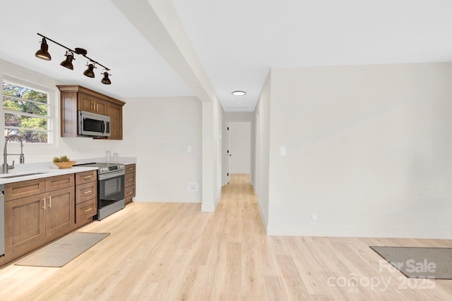 kitchen with baseboards, light countertops, light wood-type flooring, appliances with stainless steel finishes, and a sink