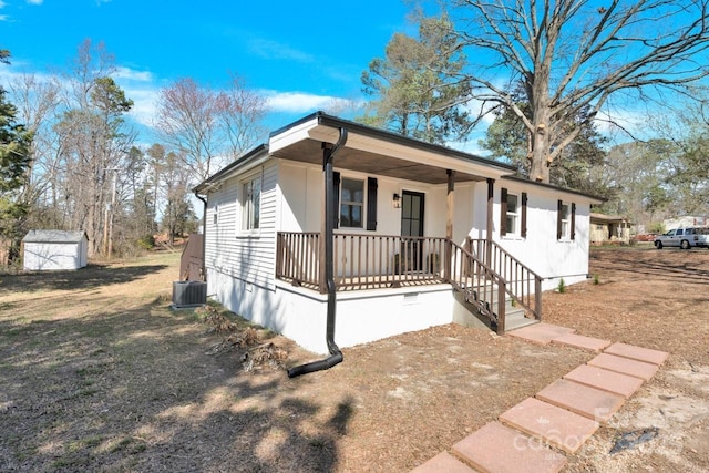 view of front of property with a porch, cooling unit, crawl space, a storage unit, and an outbuilding