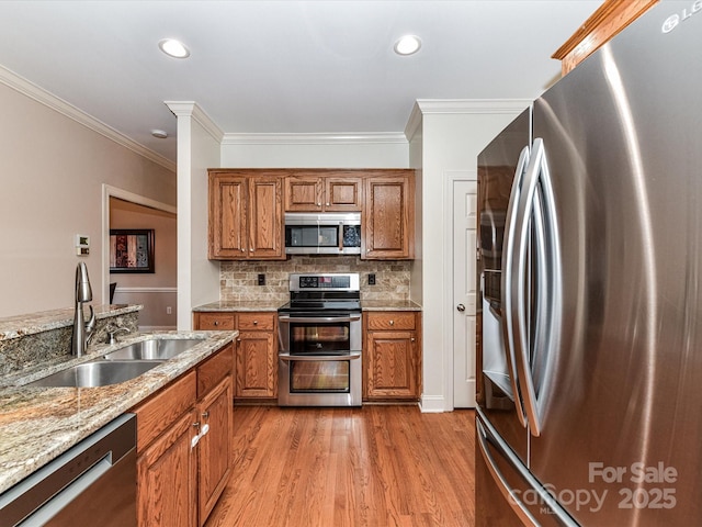 kitchen with tasteful backsplash, light wood-style floors, brown cabinetry, stainless steel appliances, and a sink