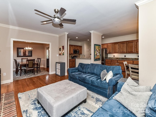 living room with ceiling fan with notable chandelier, crown molding, baseboards, and wood finished floors