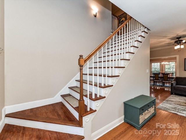 staircase with a ceiling fan, wood finished floors, baseboards, and ornamental molding