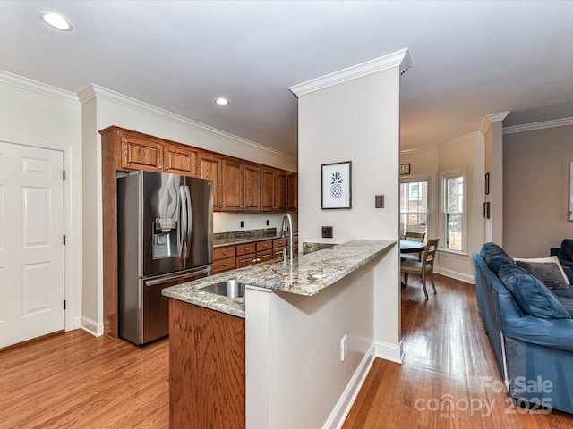 kitchen featuring brown cabinetry, a peninsula, stainless steel fridge with ice dispenser, a sink, and open floor plan