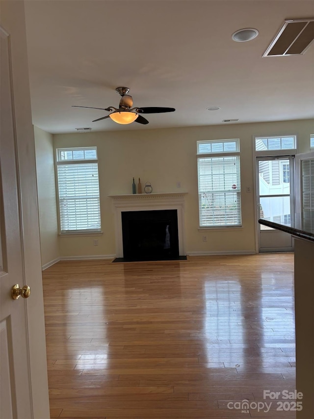 unfurnished living room featuring visible vents, baseboards, a fireplace with flush hearth, light wood-type flooring, and a ceiling fan