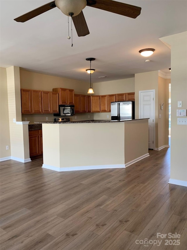 kitchen with stainless steel appliances, dark countertops, wood finished floors, and brown cabinetry